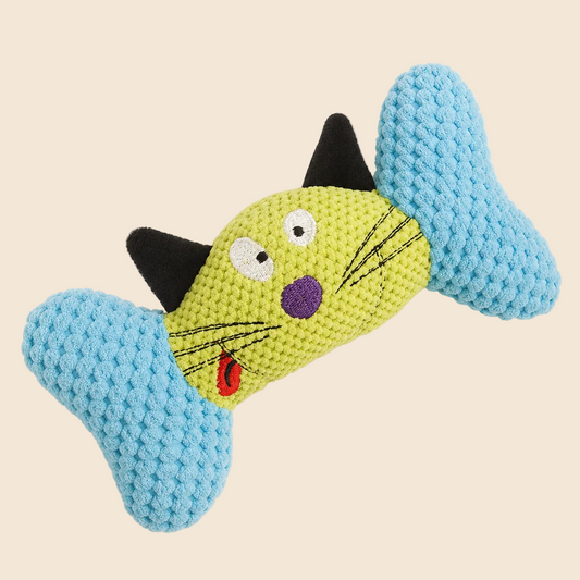 A knitted cat-shaped dog toy shaped like a bone, featuring a lime green body, light blue ends, black ears, and embroidered facial details including white eyes, a purple nose, black whiskers, and a red tongue, shown on a plain off-white background.