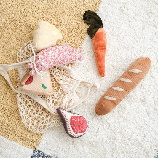 Set of handcrafted wooden toys shaped like vegetables and a bag on a textured surface.