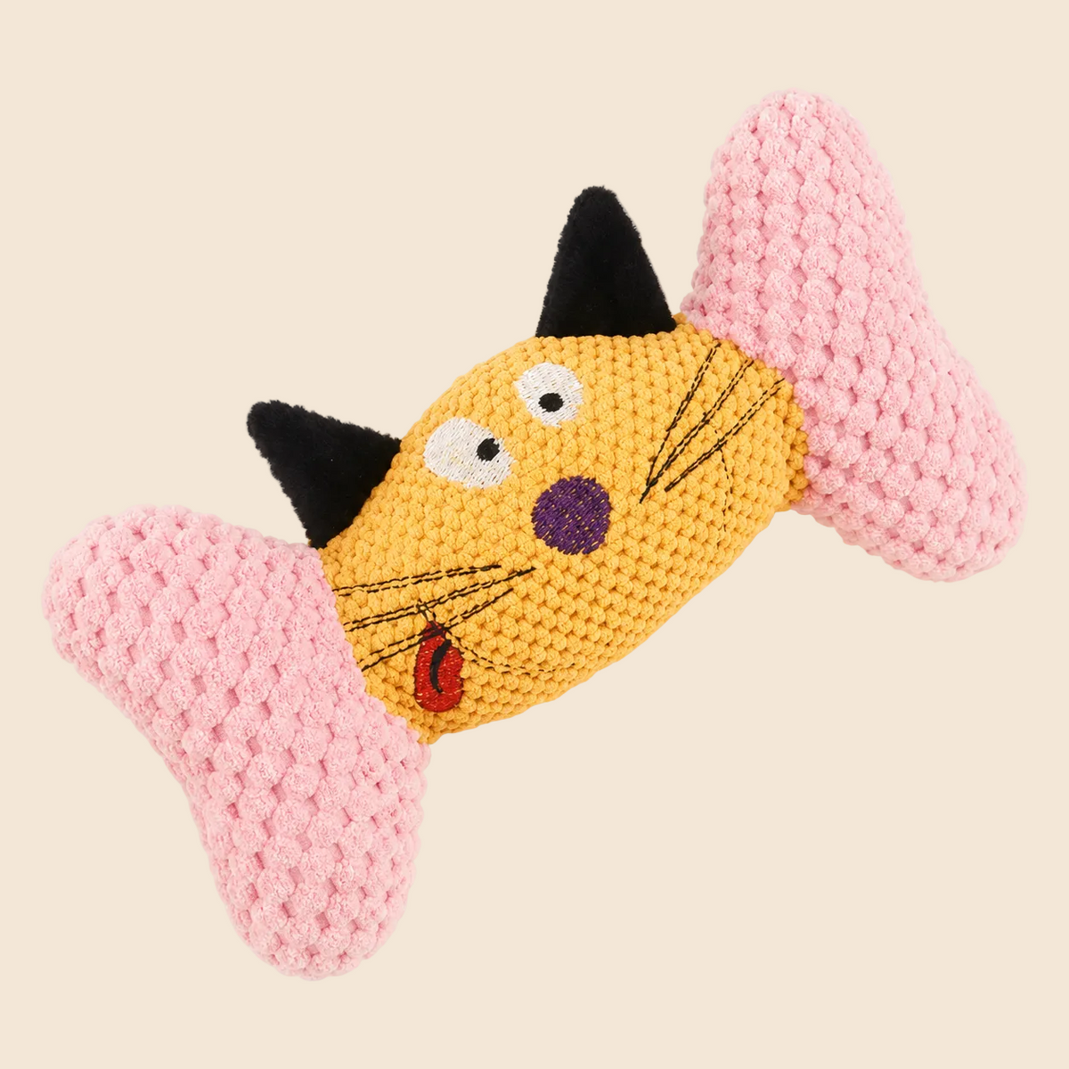 A crocheted cat-shaped dog toy with a yellow body, pink ears and tail, black ears, and embroidered facial features on a light cream background.