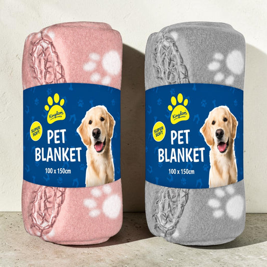 Two rolled pet blankets displayed side by side on a light surface against a textured wall. The left blanket is pink with a paw print pattern and a blue label featuring a golden retriever.