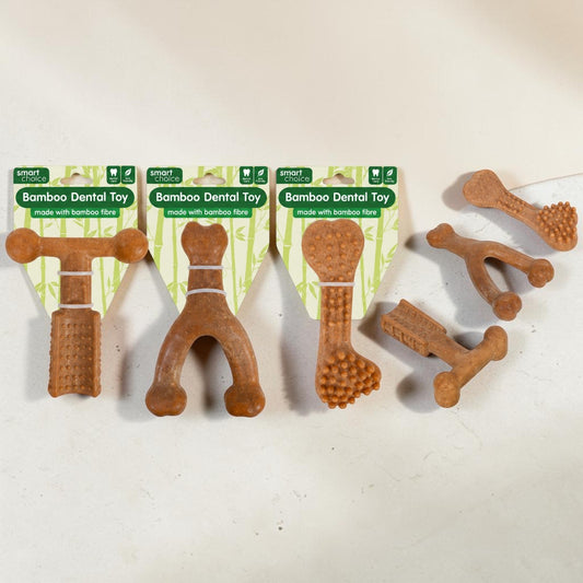 Four brown bamboo dental toys for dogs displayed on a light beige surface, with three still in their green and white cardboard packaging and one loose.