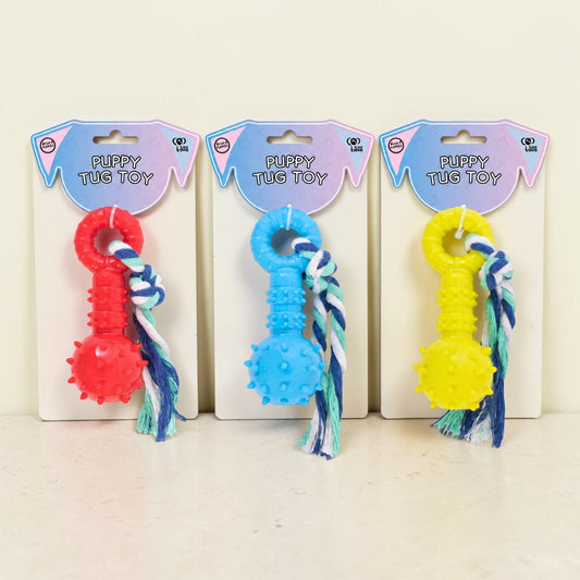 Three dog tug toys on retail backing cards, shown in red, blue, and yellow. Each toy has a textured rubber ball and a braided rope tail, with 'PUPPY TUG TOY' printed on the cards.