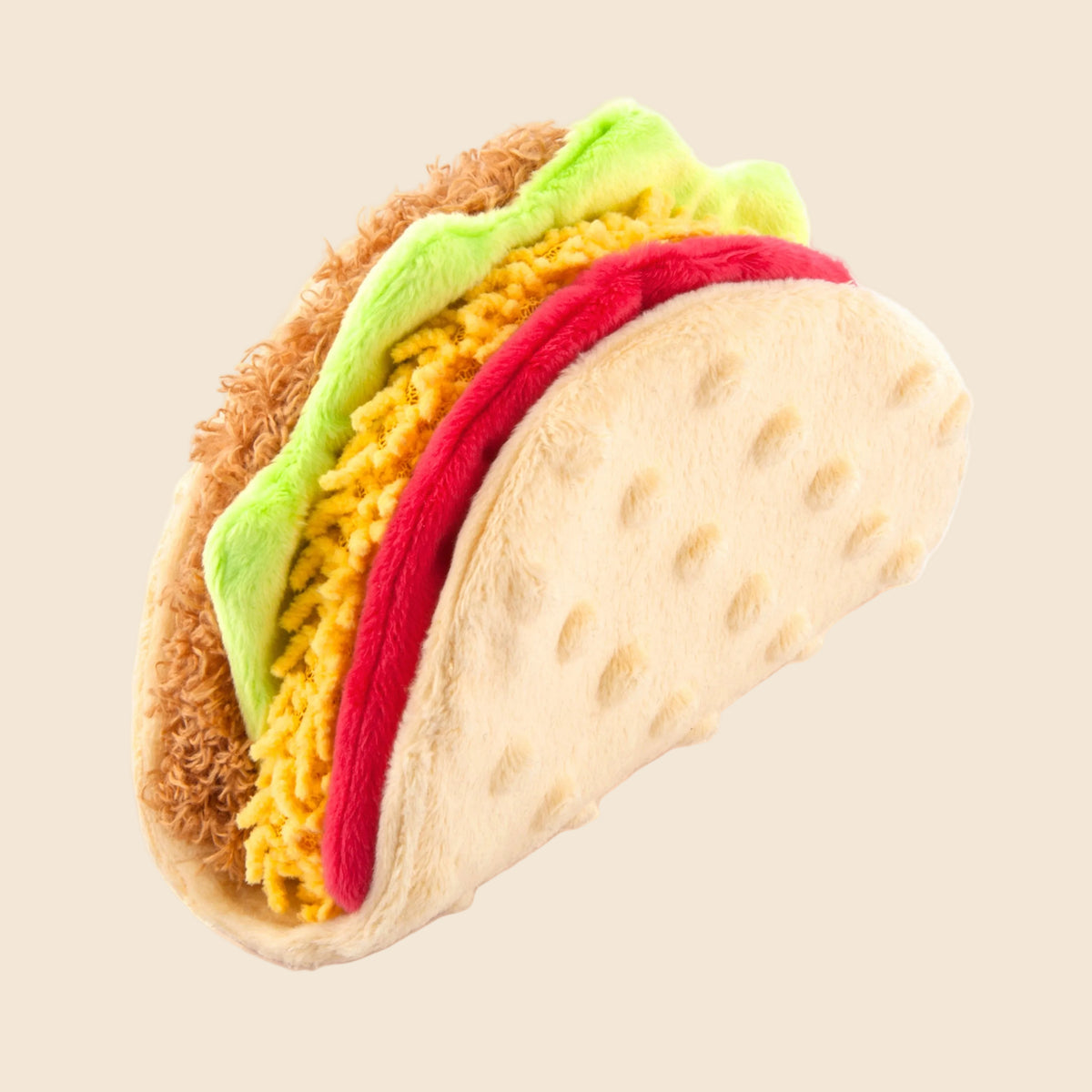 A plush novelty taco toy with textured faux-taco shell, yellow shredded filling, green lettuce, and red tomato layers on a plain beige background.