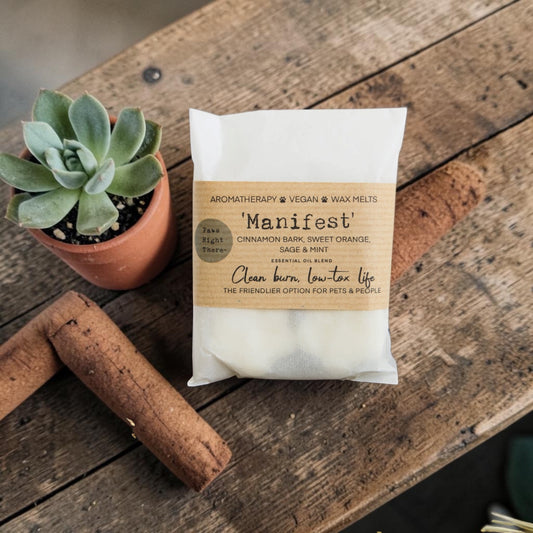 Package of 'Manifest' wax melts on a wooden surface with a potted succulent and wooden candle.