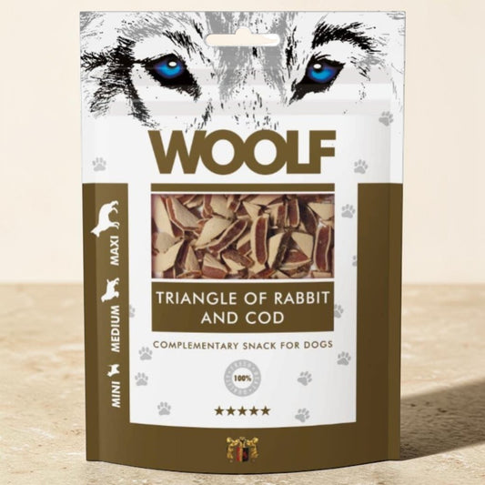 A stand-up pouch of WOOLF brand dog treats, specifically 'Triangle of Rabbit and Cod' complementary snack for dogs. The packaging features a stylized graphic of a wolf's face with bright blue eyes at the top, brown and white color blocks, and a clear window showing the triangular fish-shaped treats inside.