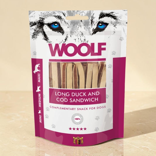 A package of WOOLF Long Duck and Cod Sandwich dog treats, featuring a white and magenta stand-up pouch with a wolf graphic and a clear window showing the wooden sticks inside.