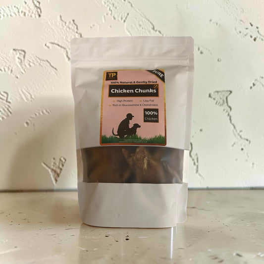 A stand-up pouch of TP Brand Chicken Chunks dog treats, featuring a clear window showing the brown treats inside, set against a textured off-white wall.
