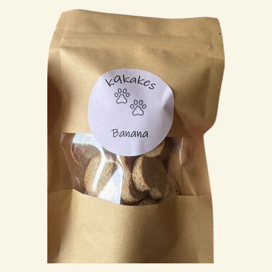 K9Kakes handmade Banana Bites dog biscuits in a brown kraft resealable pouch with a clear window showing the treats.