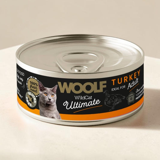 A can of Wolf WildCat Ultimate Turkey Adult wet cat food, featuring a black and orange label with a photo of a gray cat, set on a light beige surface.