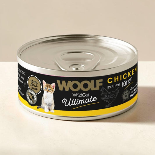 A can of Wolf WildCat Ultimate Chicken wet cat food, featuring a black label with yellow and white text, a photo of a kitten, and a chicken illustration, set against a neutral beige background.