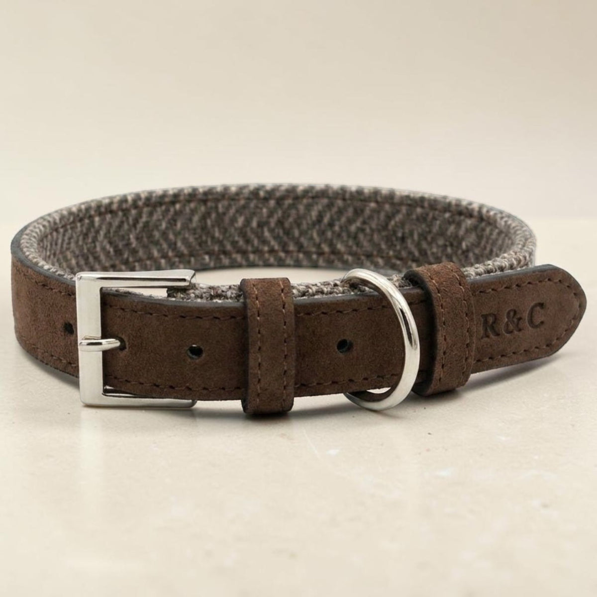 A brown leather dog collar with a textured gray and white houndstooth pattern inner band, a silver-tone buckle, and a silver-tone D-ring. The brand name 'R & C' is embossed on the leather tip.