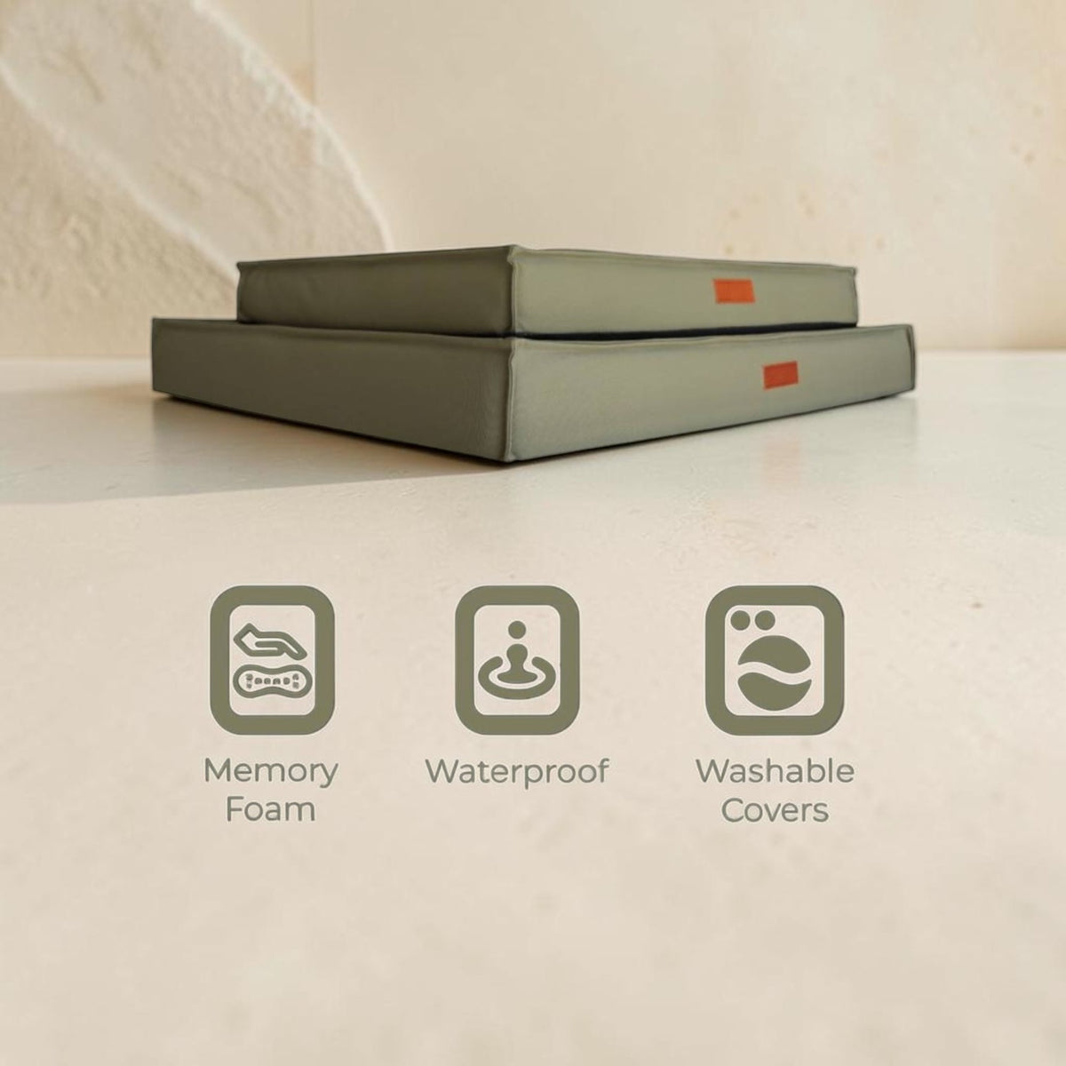 Two gray cushioned mattress toppers stacked on a light beige surface, with three feature icons and text below reading Memory Foam, Waterproof, and Washable Covers.