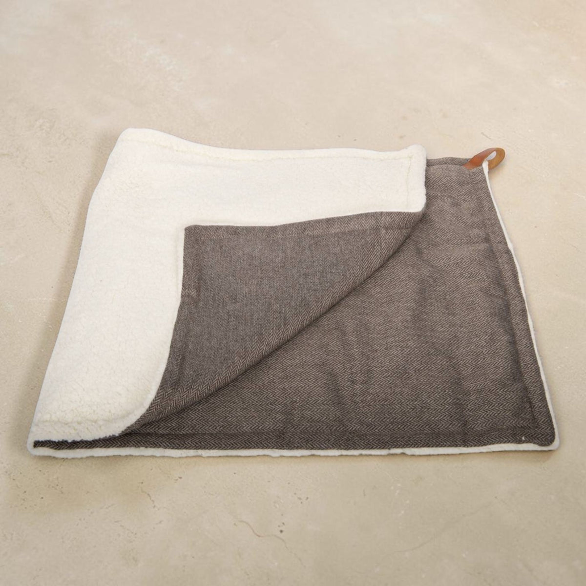 A folded rectangular towel or blanket with a textured brown woven front and a soft off-white fleece backing, shown on a light beige stone-like surface.
