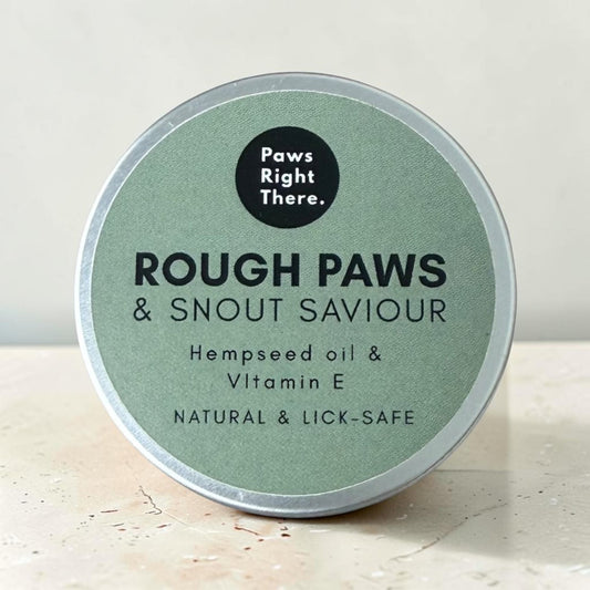A round silver tin of Paws Right There. Rough Paws & Snout Saviour lick mat, featuring a sage green label with black text, set on a light beige stone surface.