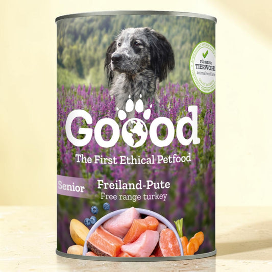 A can of Goood Senior Freiland-Pute dog food, featuring a label with a dog in a purple flower field, salmon and blueberries, and a 'Tierwohlethik' seal, set against a light beige background.