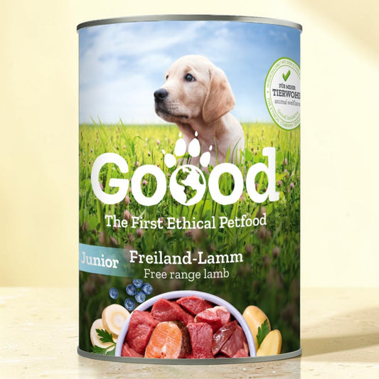A can of Goood Junior Freiland-Lamm dog food, featuring a label with a golden retriever puppy in a green field and a bowl of raw lamb meat at the bottom, set against a light beige background.