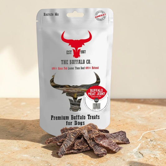 A stand-up pouch of The Buffalo Co. Premium Buffalo Treats for Dogs, shown on a stone surface with several pieces of dried jerky in front.