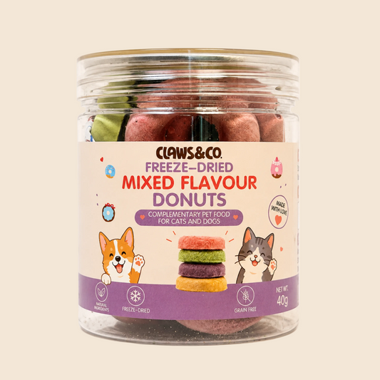 A clear plastic jar of Claws & Co. Freeze-Dried Mixed Flavour Donuts for cats and dogs, filled with pinkish-brown freeze-dried donuts, set against a solid light beige background.