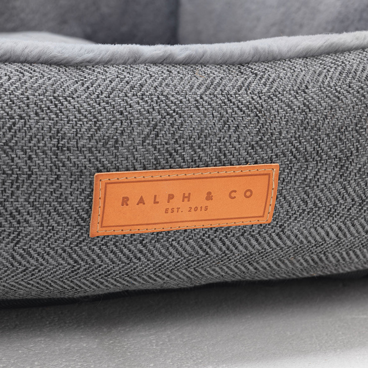 Gray textured pet bed with a brown leather label reading 'Ralph & Co' on a gray background.