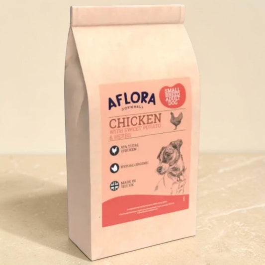 A bag of Aflora Cornwall Chicken wet and dry dog food, featuring a pale pink package with a red and blue label, set against a neutral beige background.