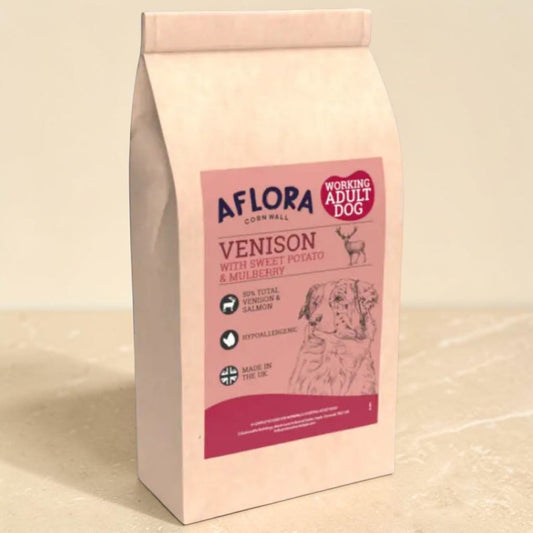 A bag of Aflora Corn Hall Venison dog food for working adult dogs, featuring a pink and magenta label with a dog illustration, set against a neutral beige background.