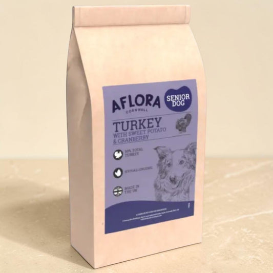 A bag of Aflora Cornwall Senior Dog food, Turkey with Sweet Potato & Cranberry, standing on a beige surface against a matching beige background.