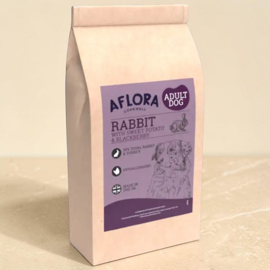 A bag of Aflora Cornwall Adult Dog Rabbit food, featuring a light beige stand-up pouch with a purple label, set against a neutral beige background.